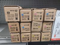 Stack of Xerox toner cartridge boxes showing various colors (K, C, M, Y) and quantity totaling 12 cartridges.