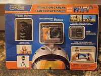 Front of packaging showing Explore One HD Action Camera with WiFi, waterproof case, tripod mount, 8GB micro SD card, and connectivity features.