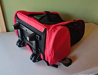 View of red backpack pet carrier resting on its side showing black wheels on bottom and a ventilation mesh top.