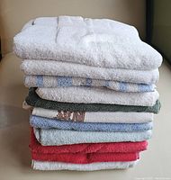 Stack of assorted bath towels in various colors including white, blue, green, red and pattern designs