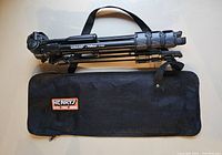 Folded Henry Velbon HTB-4 tripod placed on top of a black carrying case with shoulder strap and Henry's logo patch visible.