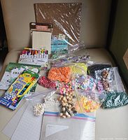 Overview showing a large assortment of craft supplies including markers, crayons, multiple bags of beads in various colors and sizes, plastic canvas sheets and cork board sheets