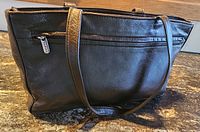 Front view showing full handbag with two handles and external zipped pocket.