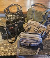 Photo showing five handbags and purses of various colors and designs on carpet and wooden background.