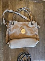 Beige Michael Kors handbag lying flat on wooden surface showing front and handles with crocodile-textured trim and shoulder strap.