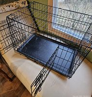 Showing large black wire pet crate with front door open and black plastic tray bottom.