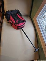Image showing the red and black rolling backpack lying flat with extended handle on a light colored surface near a window.