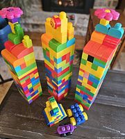 Three large towers made from colorful Mega Bloks, each topped with a flower piece, alongside four smaller assembled block models resembling vehicles and animals.