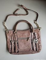Front view of the Michael Kors handbag showing the leather exterior, front zipper pocket, dual handles, adjustable shoulder strap with chain details, and MK charm.