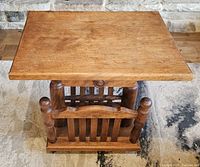 Front perspective showing the top table surface and magazine rack compartments beneath, highlighting the turned wood posts and vertical slats.