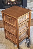 Front angled view of small table with wooden top and 3 wicker drawers fitted into wood frame.