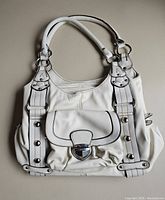 Front view of the white leather handbag showing dual handles, front flap pocket with metallic clasp, and buckle details.