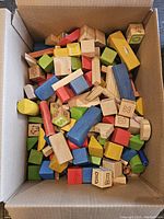 Box filled with assorted wooden blocks in multiple colors and shapes, some with letters and symbols.
