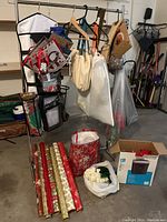 Wide view showing Christmas wrapping paper rolls, hanging gift bags, plastic bags with greenery, and a box containing decorations on a metal rack.