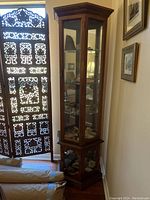 Full view of the tall wooden corner curio cabinet with glass paneled doors and interior lighting visible inside.