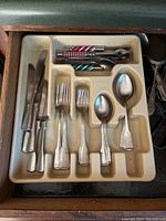 Plastic tray holding a set of basic metal silverware, including knives, forks, and spoons, arranged neatly.