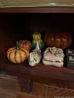 Five ceramic decorative pumpkins and a ceramic figurine resembling a chef on a shelf