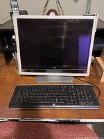 HP square LCD monitor with silver bezel and base, placed on a wooden desk with HP wired keyboard in front.
