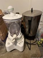 Photo of white electric blender and large stainless steel coffee percolator on a surface