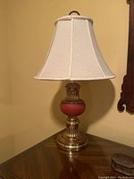 Full view of the antique medium table lamp on a wooden table, showing the fabric bell-shaped lampshade and base with brass and red components.
