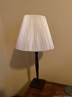 Full view of small antique table lamp with beige fabric lampshade and dark brown base on a wooden surface