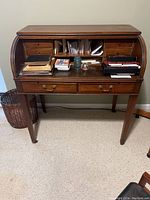Front view of roll top desk with workspace open showing small drawers and cubbyholes inside, containing various papers and small items.