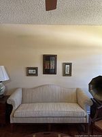Full shot of cream-colored sofa against a wall with three framed pictures above. Sofa has wooden legs and arm accents.