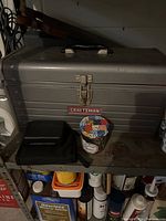 Closed metal Craftsman toolbox with small black case and container on front shelf