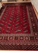 Full view of rectangular rich red wool area rug with medallion and floral pattern and multiple decorative borders on hardwood floor.
