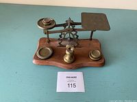 Full frontal view of the small wooden and brass Victorian postal scale on a blue surface with identification card in front.