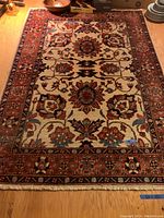 Top-down view of full area rug laid on wooden floor, showing main design and colors including rust, navy, green on off-white background.