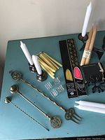 Overview of candle holders, brass snuffers, various loose tapers, and packaged tapers arranged on a blue table surface.