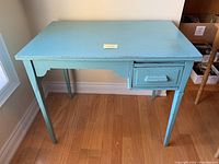 Front view of the solid wood chippy blue painted antique desk showing rectangular top, slender legs and right drawer.