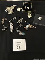 Complete collection of 12 brooches and earring studs arranged on black fabric, showing all items in the lot.