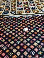 Both crochet throw blankets displayed together; shows large beige background blanket with earth tone squares on top and smaller deep purple background blanket with multi-color accents beneath.