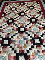 Full view of the double-sized patchwork quilt showing the colorful small squares, dark blue framing squares, and red border