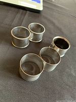 Five silver napkin rings arranged on black fabric, showing overall set