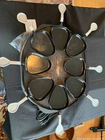 Top-down view of round raclette grill with 8 raclette dishes and handles visible, on black table.