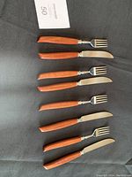 Full set laid out showing four forks and four knives with teak wood handles on black fabric.
