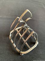 View of the silver plated toast holder from a 45-degree angle showing its open frame, handle, and ball feet.