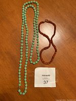 Two necklaces laid on wood surface, showing the full length of the green glass bead necklace and the amber bead necklace with bayonet clasp.