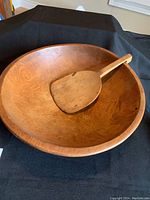 Angled view of the wooden bowl with paddle inside showing wood grain and size proportions.
