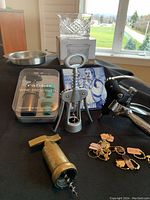 Photo showing two bottle coasters (one crystal, one stainless steel), a Rabbit wine preserver pump in packaging, three corkscrews including Rabbit Ear style and traditional, wine stem charms, and a square sommelier trivet.