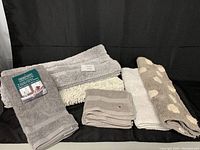 Six bath mats and hand towels displayed, showing two large mats, two smaller spotted mats, Tommy Hilfiger towels, and Serenity towels with tags.