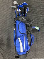 Full view of the blue and black children's golf bag with shoulder strap and built-in stand, laying horizontally.
