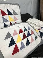 Double quilt and matching quilt pillow covers displayed showing the colorful triangle patch design against a white quilted background.
