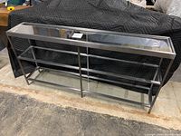 Front view of the metal and glass console table showing metal frame and three glass shelves.