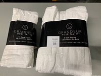 Photo showing pack of 10 white hand towels and pack of 5 white bath towels in original packaging with black Grandeur Hospitality bands.