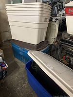 Stack of tan Rubbermaid storage totes with beige lids on top and a blue Rubbermaid tote with a brown lid underneath.