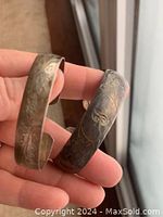 Photo showing two tarnished sterling silver cuff bracelets held in hand, revealing engraved vine and floral patterns.
